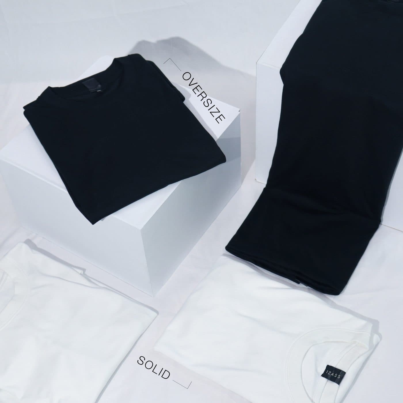 เสื้อยืดโอเวอร์ไซซ์สีดำและขาวพับวางบนกล่อง พร้อมป้ายแท็กกระดาษ